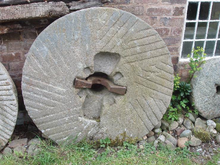 An antique millstone leaning against a barn